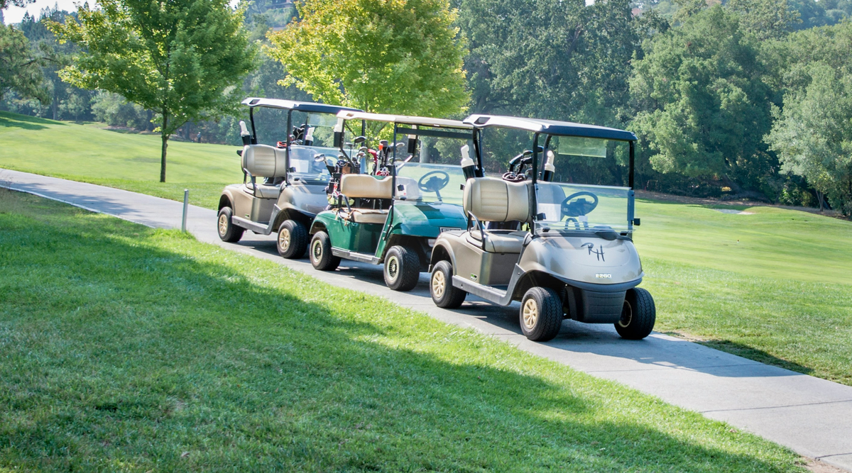 Three golf carts in the sunshine on a golf course path