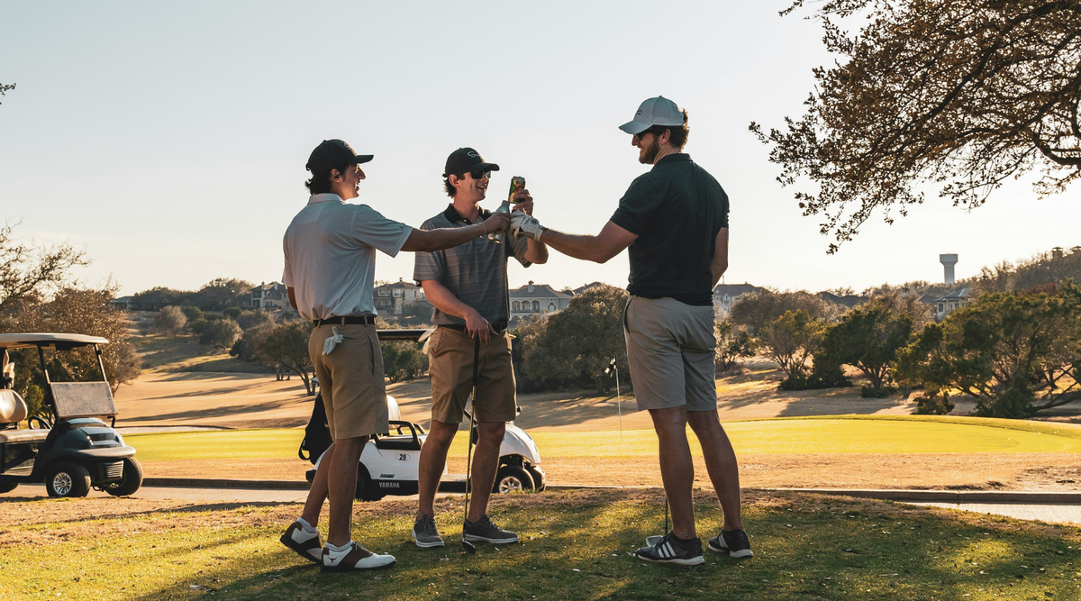 Three men toasting on the golf course in afternoon sunlight