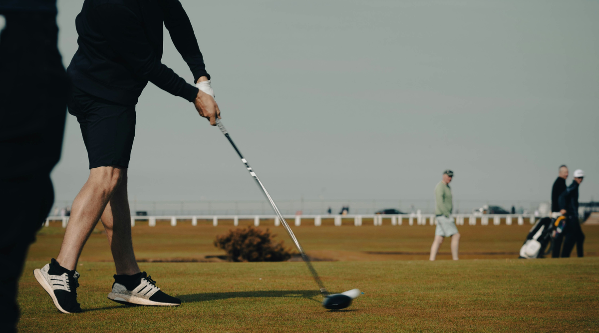 Man mid-golf swing with three friends in background