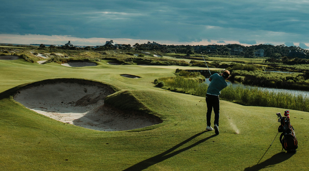 Man mid-swing on golf course facing water